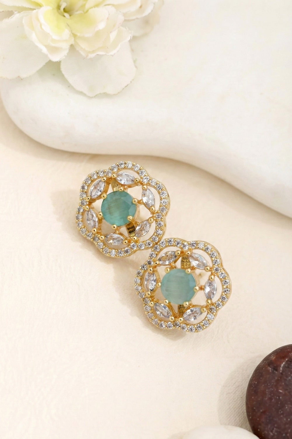 Gold earrings with mint green gemstones and cubic zirconia diamonds on a white surface with flowers.